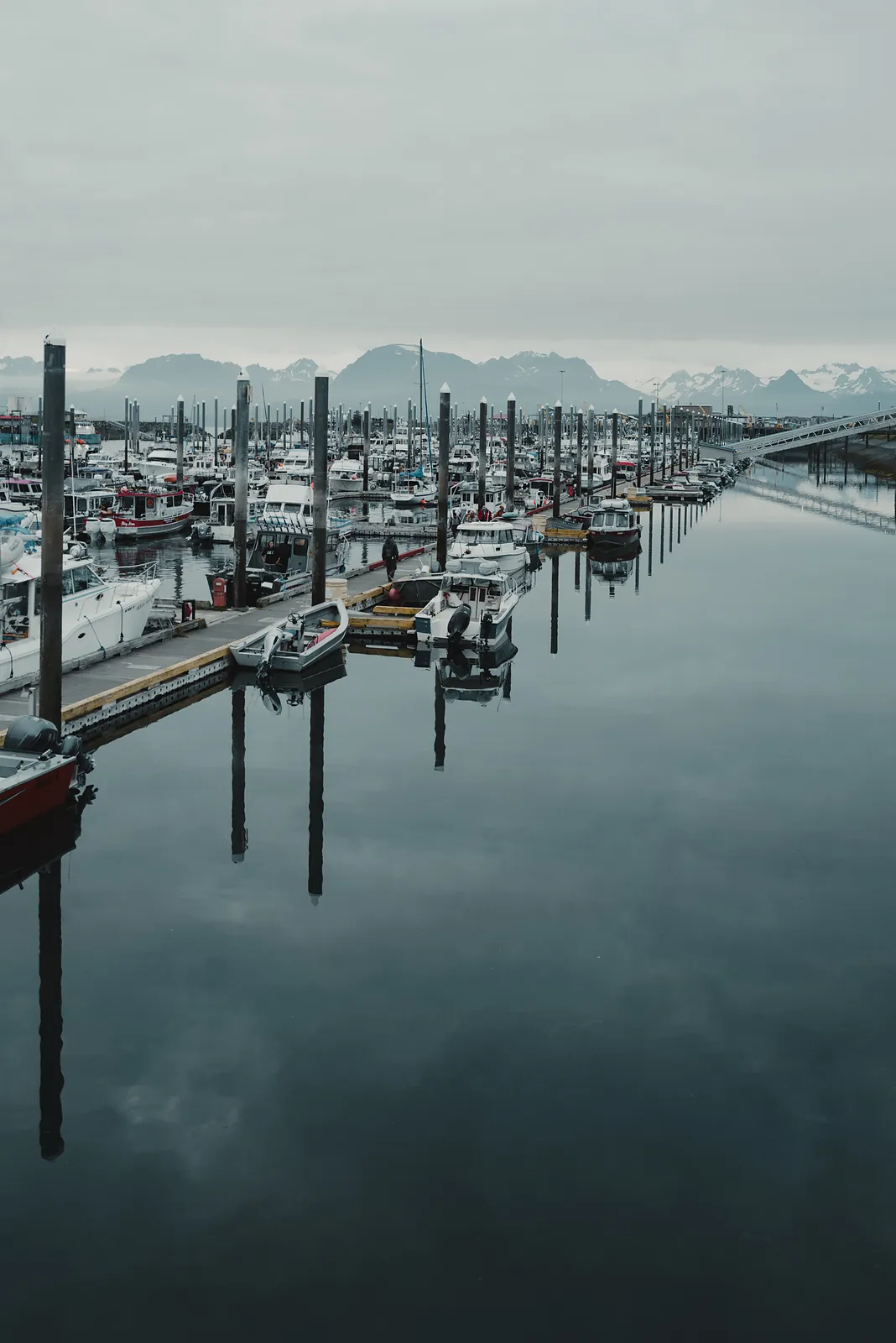 Boats moored along a still harbour channel with distant mountains in flat morning light