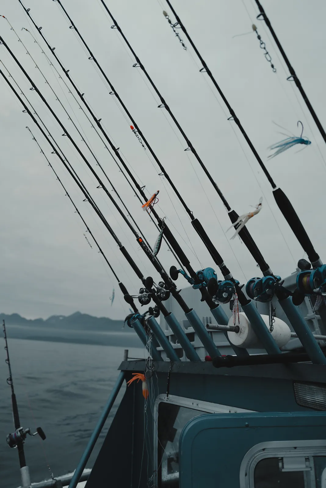 A rack of fishing rods angled against a pale grey sky aboard a charter boat
