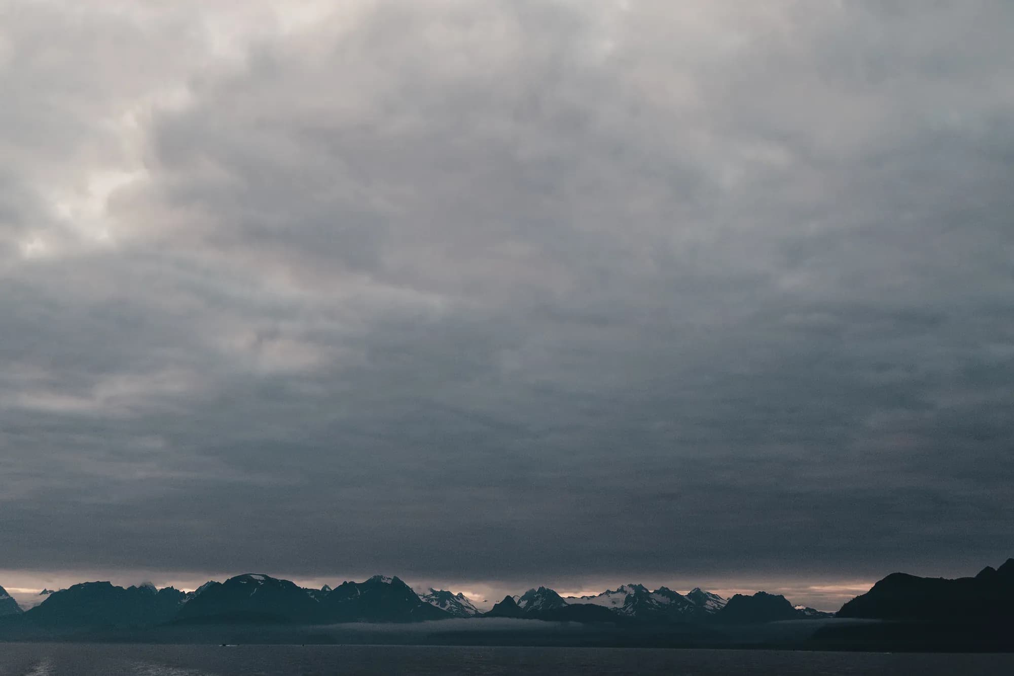 A low mountain range under heavy cloud across grey water in Kachemak Bay
