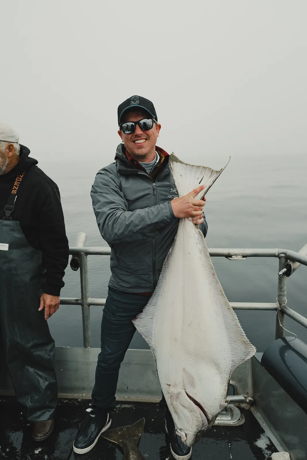 A man holding up a large flat halibut by the rail of a charter boat