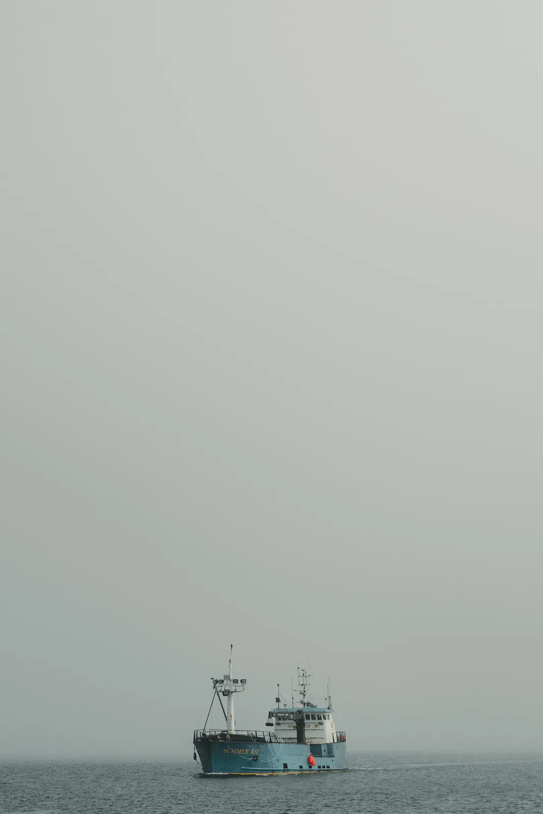 A small blue fishing tender crossing flat grey water in heavy fog