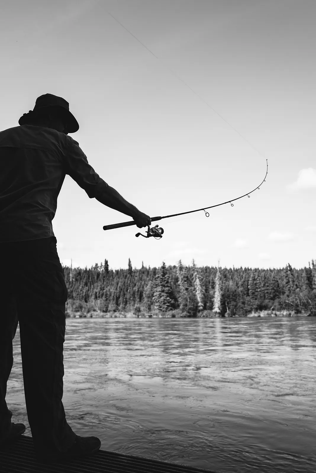 A silhouetted figure casting a fishing rod against a bright open sky