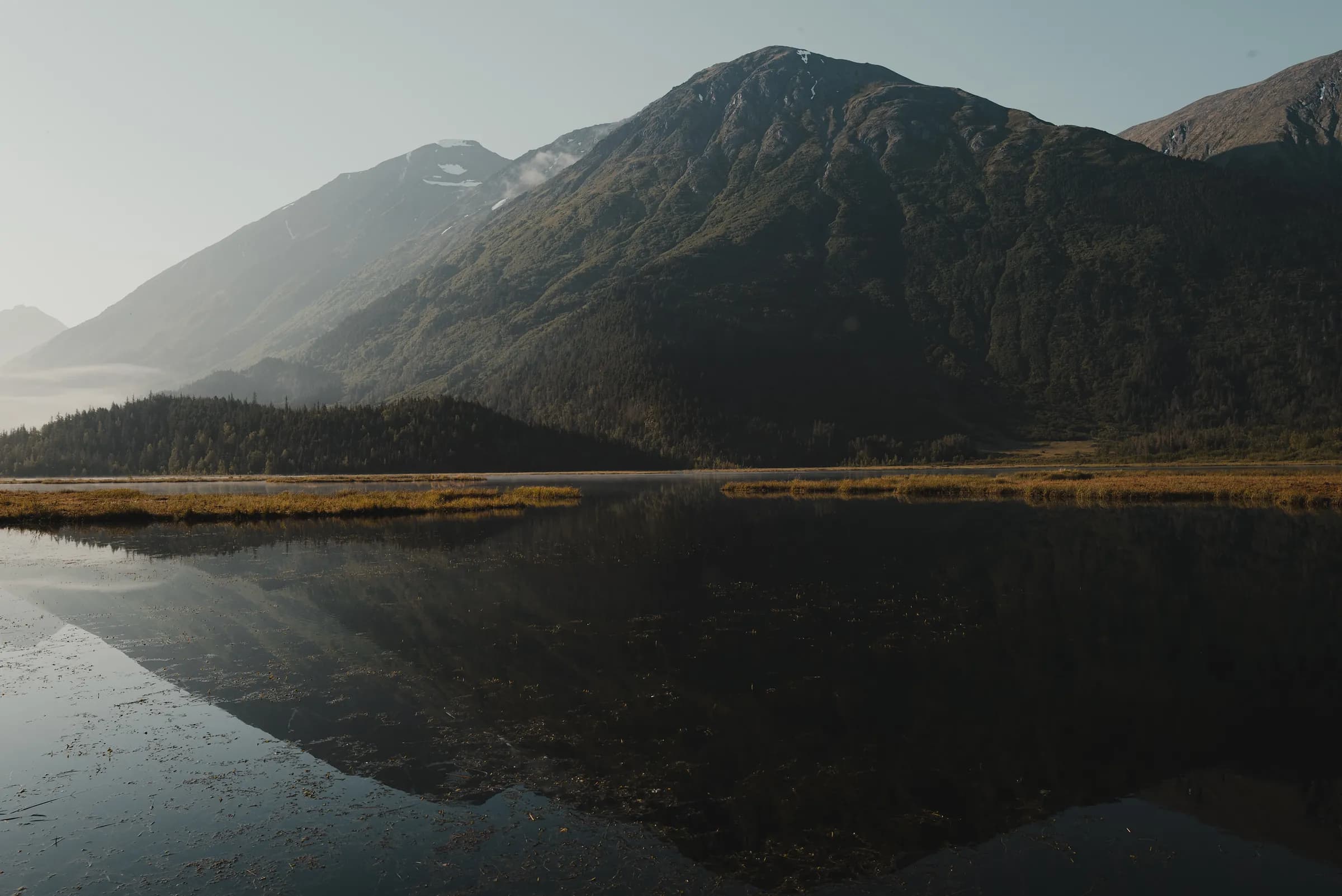 Mountains and spruce forest reflected in the still water of Tern Lake with low cloud in the trees