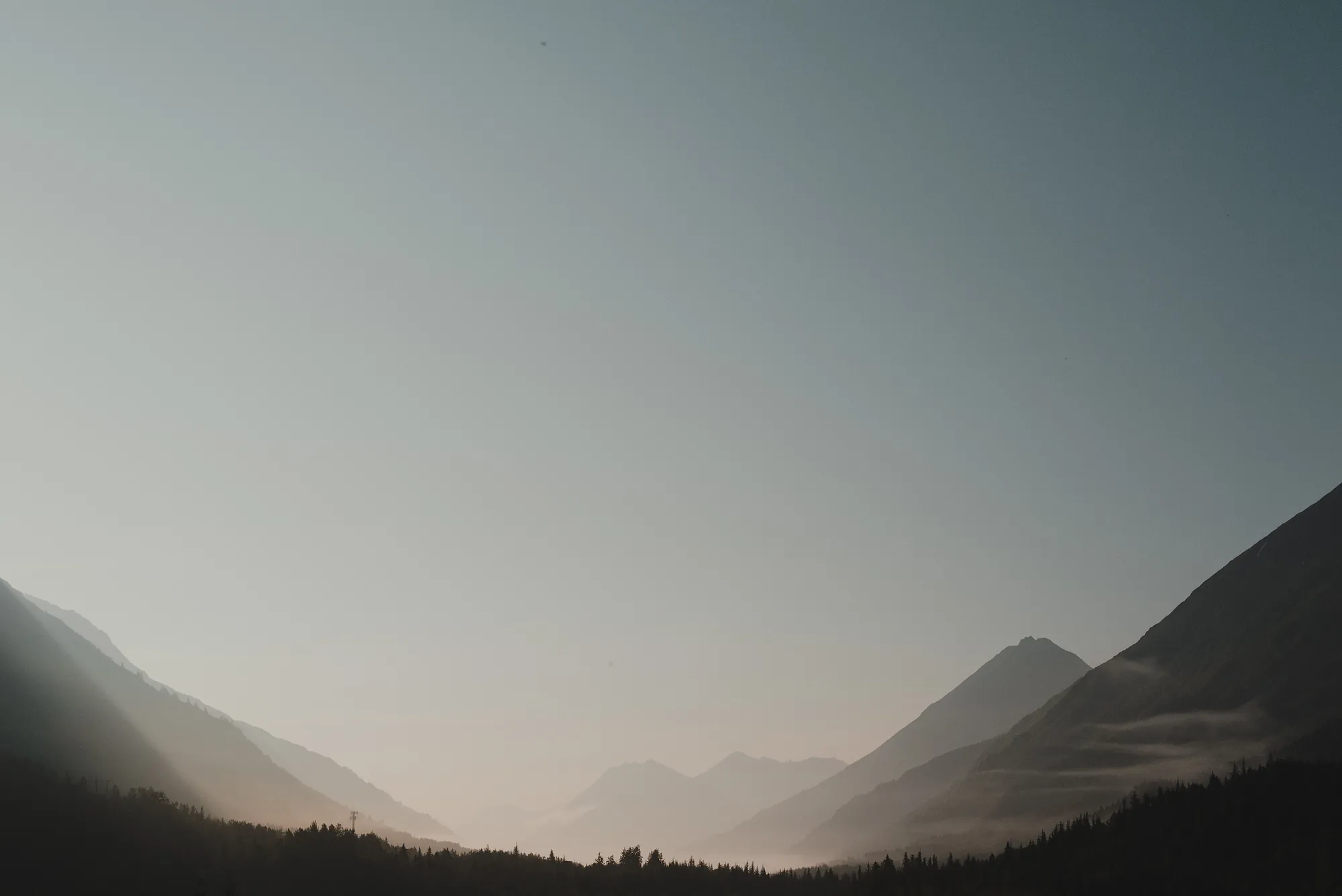 Layered mountain ridges fading into haze above a dark forested valley