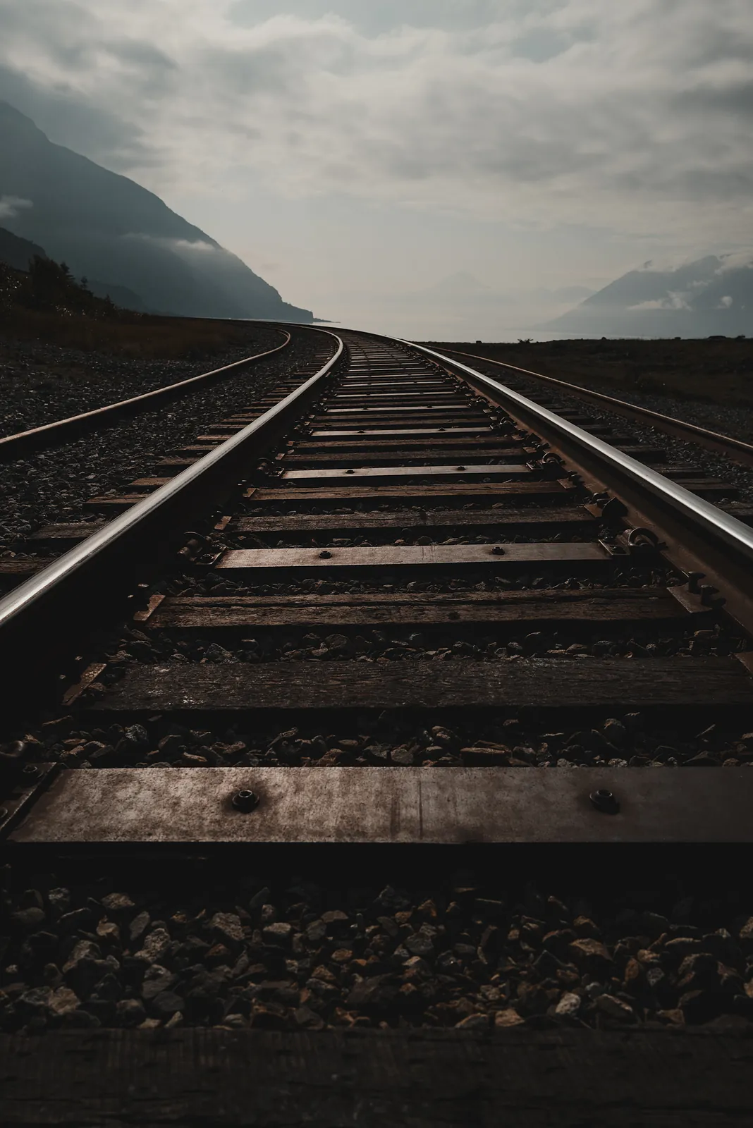 Railroad tracks running away toward mountains under a pale overcast sky